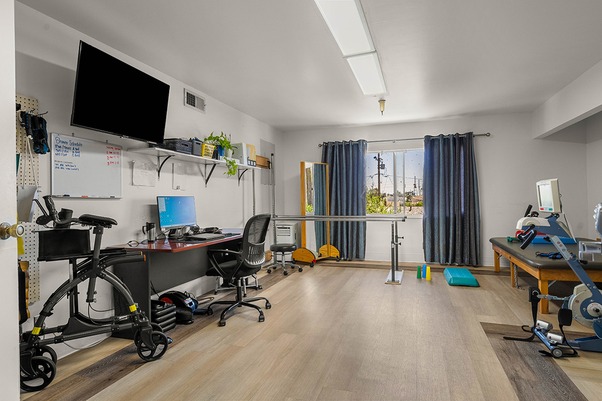 Bright rehabilitation room with exercise equipment and workspace.