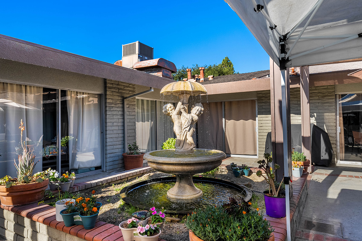 Fountain surrounded by flowers in a sunny courtyard.